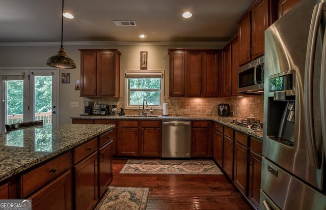 kitchen with appliances with stainless steel finishes, a sink, ornamental molding, dark stone counters, and tasteful backsplash