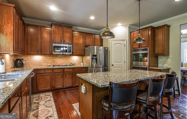 kitchen featuring stainless steel appliances, a kitchen island, ornamental molding, light stone counters, and dark wood-style flooring