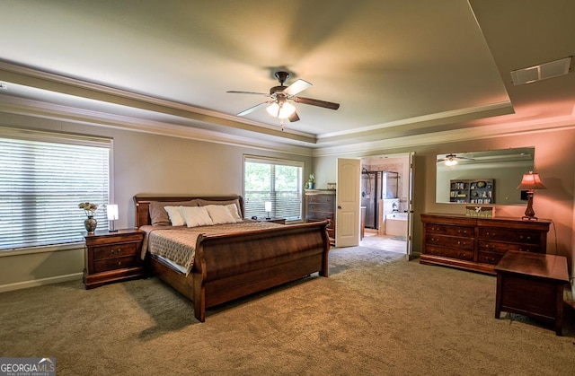 carpeted bedroom with a raised ceiling, ornamental molding, baseboards, ensuite bathroom, and ceiling fan