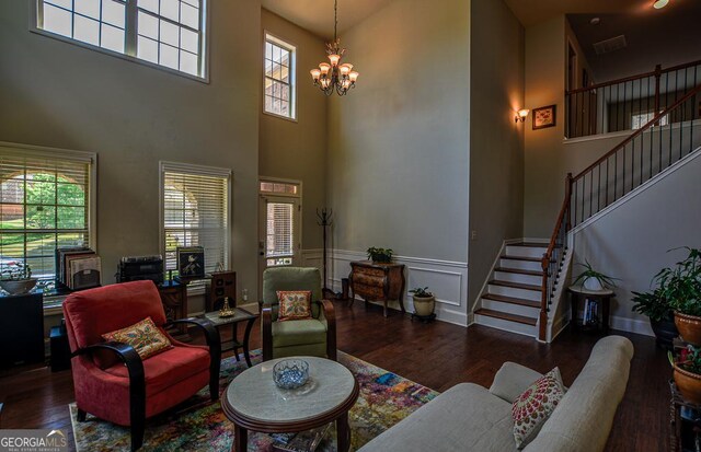 living area featuring a towering ceiling, stairway, wood finished floors, a chandelier, and baseboards