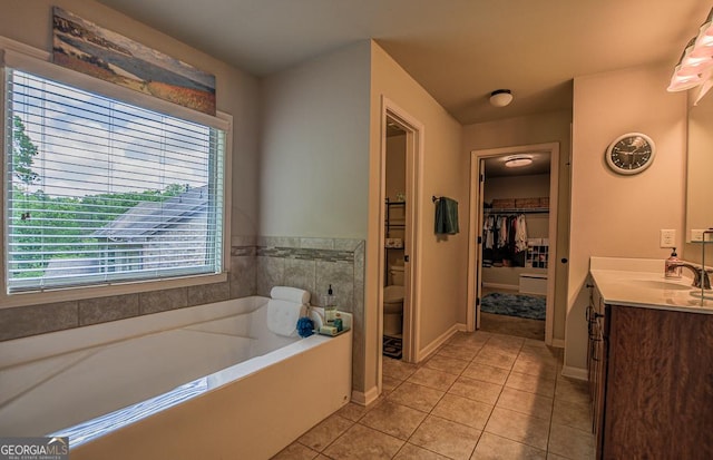 full bath featuring tile patterned flooring, a bath, vanity, a walk in closet, and baseboards