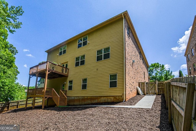 back of property with a fenced backyard, a deck, brick siding, and stairway
