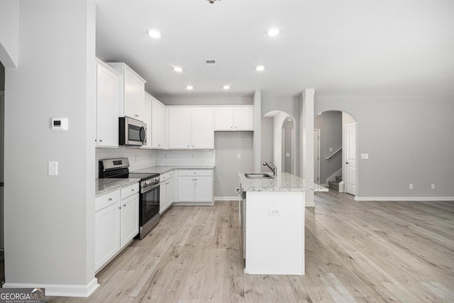 458 Ajo Way, Dallas, GA 30157 - kitchen with stainless steel appliances, light wood-type flooring, light stone countertops, backsplash, and a center island with sink