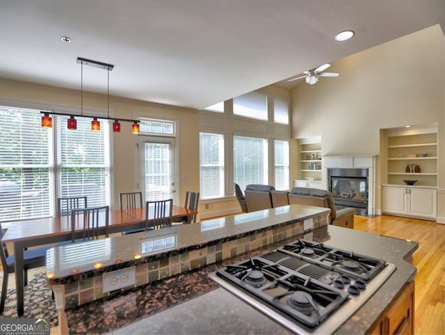 kitchen with a ceiling fan, stovetop with downdraft, a multi sided fireplace, dark stone countertops, and a towering ceiling