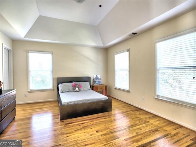 bedroom featuring a raised ceiling, light wood-style flooring, and multiple windows
