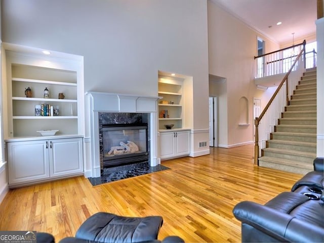 living room featuring built in features, a towering ceiling, light wood-style floors, stairway, and a fireplace