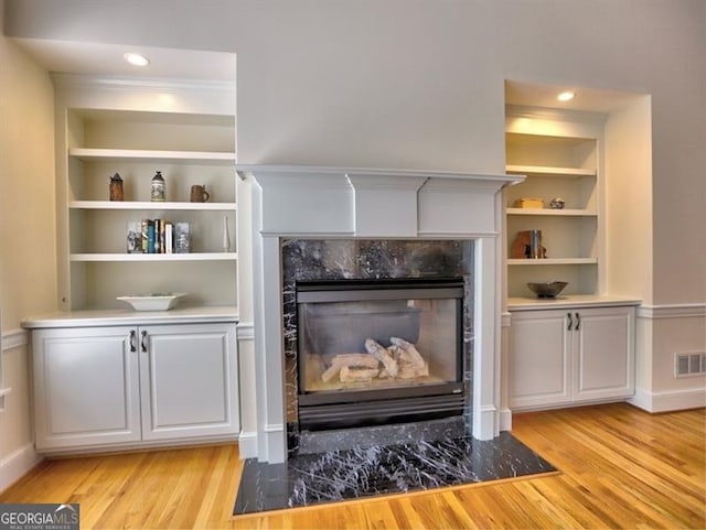 living area featuring light wood-type flooring, a premium fireplace, built in features, baseboards, and recessed lighting