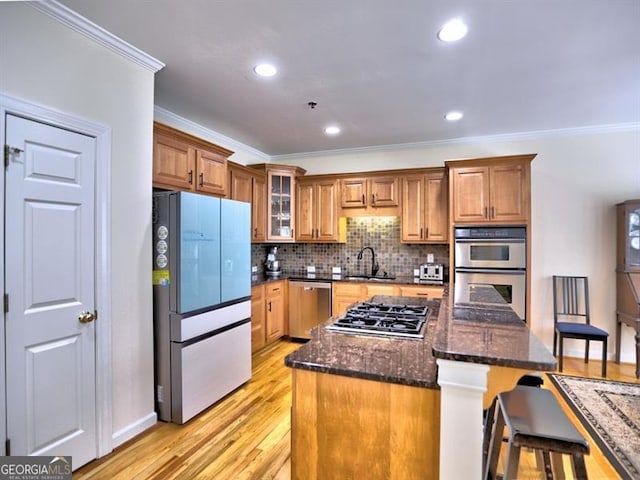 kitchen with appliances with stainless steel finishes, ornamental molding, light wood-style flooring, brown cabinetry, and a sink