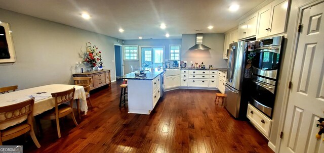 762 Old Mcleod Bridge Rd, Adrian, GA 31002 - kitchen with wall chimney exhaust hood, a breakfast bar area, white cabinets, dark wood finished floors, and stainless steel appliances