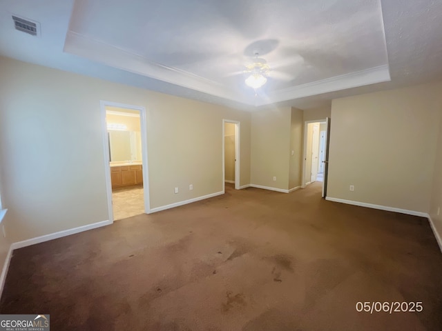 unfurnished bedroom featuring a tray ceiling, baseboards, carpet, and a walk in closet