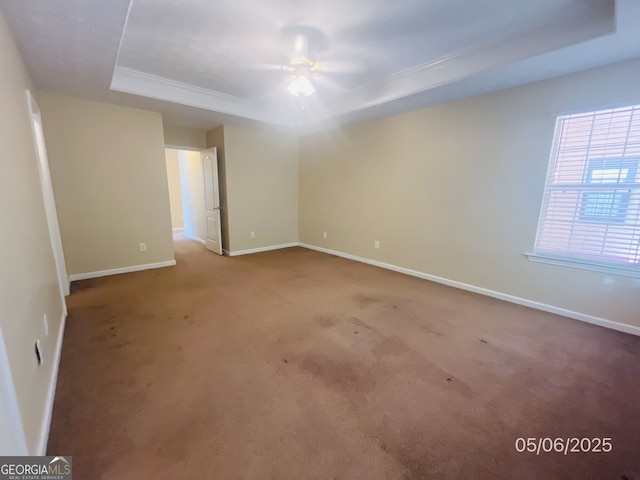 carpeted spare room featuring a tray ceiling, a ceiling fan, and baseboards