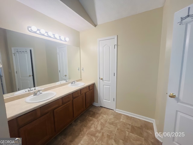 full bathroom with double vanity, baseboards, and vaulted ceiling