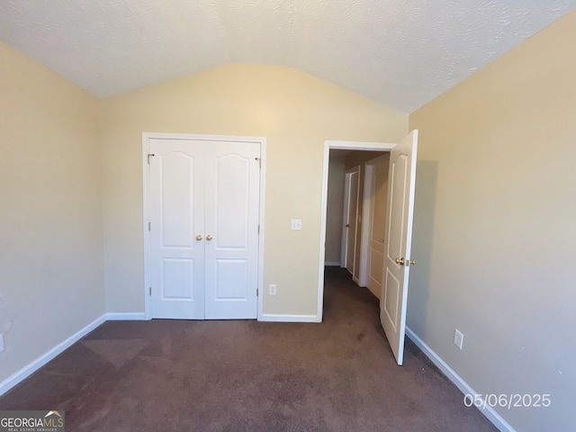 unfurnished bedroom featuring vaulted ceiling, dark carpet, and baseboards