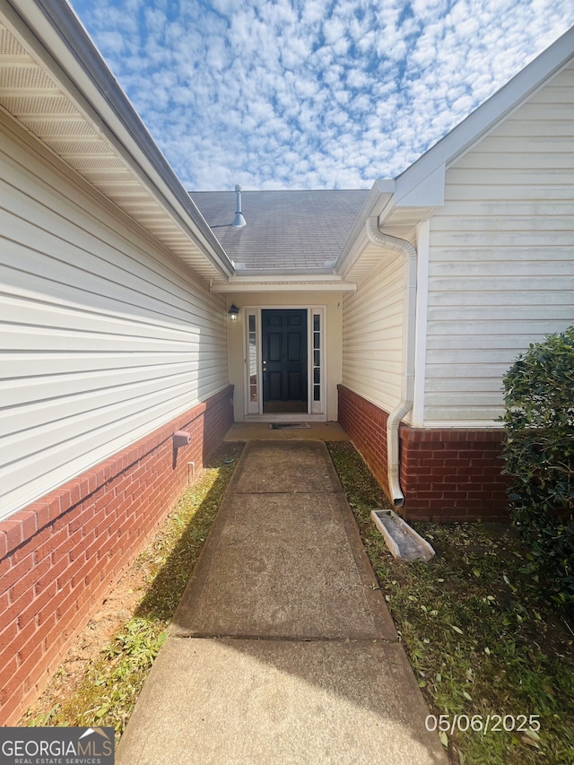 doorway to property with brick siding and roof with shingles