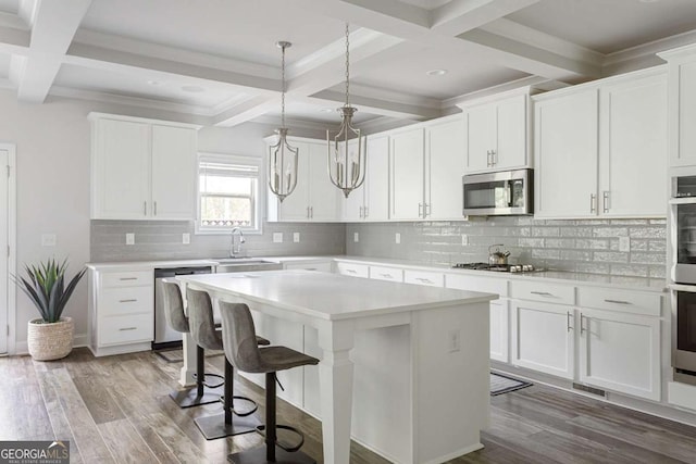 kitchen with appliances with stainless steel finishes, coffered ceiling, a sink, a center island, and beamed ceiling