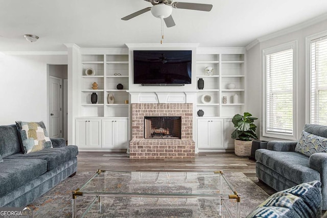 living area with ceiling fan, wood finished floors, ornamental molding, and a brick fireplace