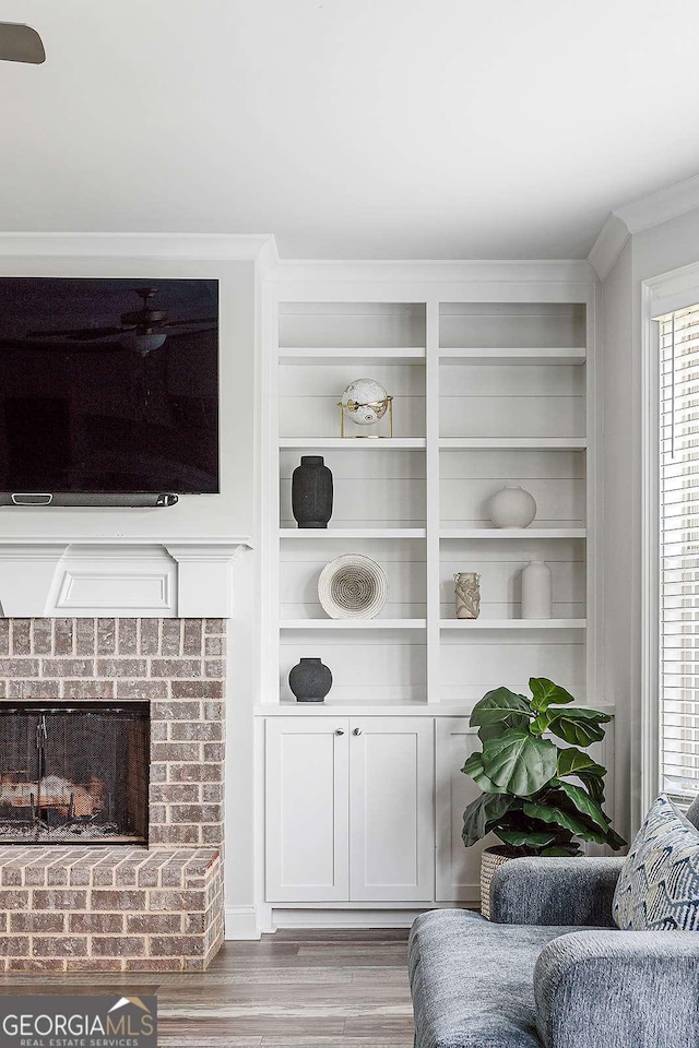 living area with light wood-style flooring, a brick fireplace, built in features, and ornamental molding