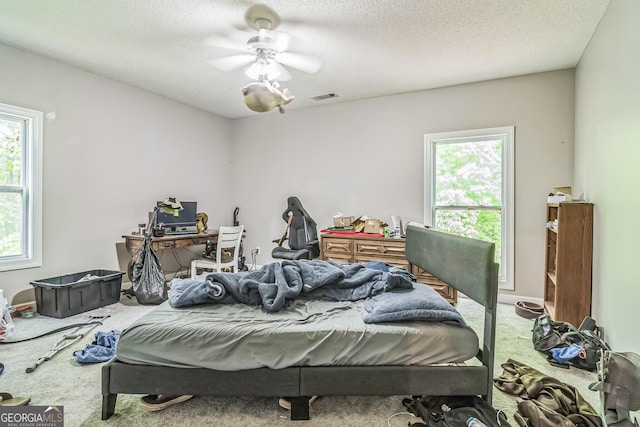carpeted bedroom featuring multiple windows, a textured ceiling, and ceiling fan