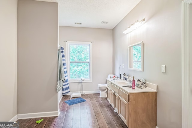 bathroom featuring healthy amount of natural light, toilet, wood finished floors, and a textured ceiling