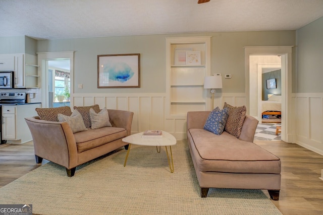 living area featuring light wood-style flooring, a wainscoted wall, and a decorative wall