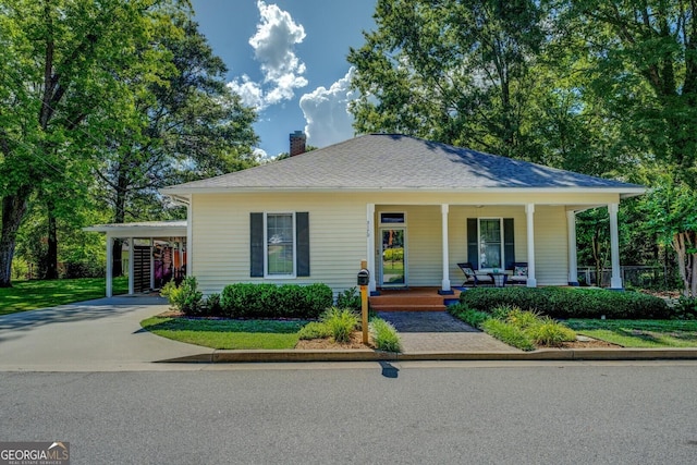 view of front of house featuring a porch, a chimney, driveway, and a carport