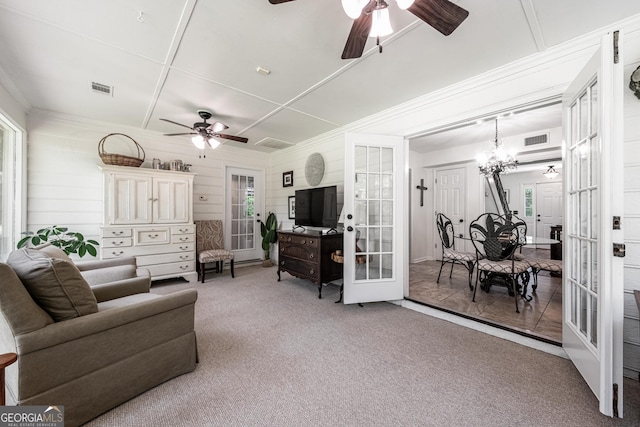 carpeted living area with french doors, ceiling fan, crown molding, and a chandelier