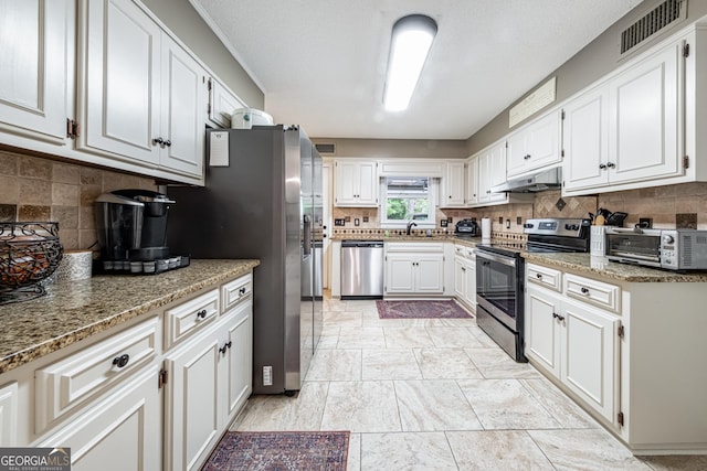 kitchen with stainless steel appliances, under cabinet range hood, a sink, decorative backsplash, and white cabinetry