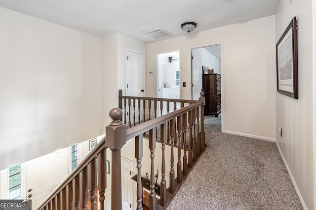 hall featuring an upstairs landing, carpet floors, baseboards, and a textured ceiling