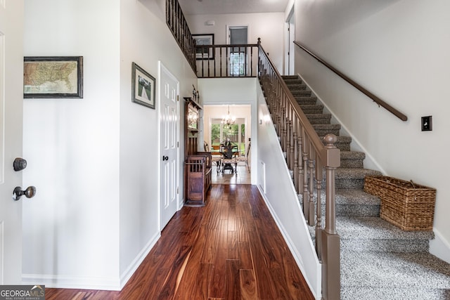 foyer entrance with stairway, wood finished floors, a chandelier, a towering ceiling, and baseboards