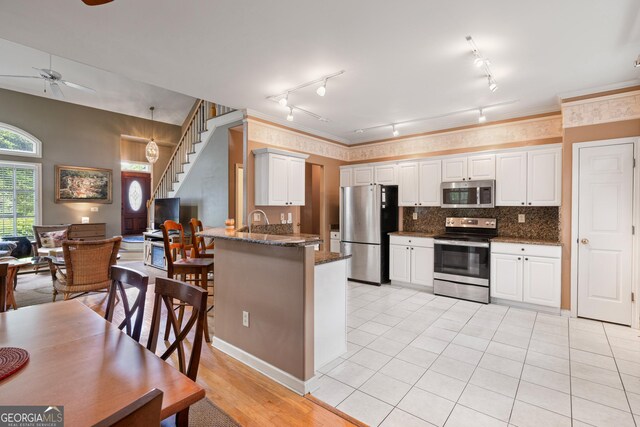 kitchen with appliances with stainless steel finishes, ceiling fan, rail lighting, a peninsula, and dark stone counters