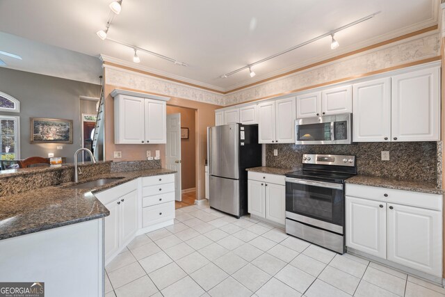 kitchen with appliances with stainless steel finishes, rail lighting, a sink, light tile patterned floors, and white cabinets