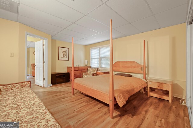 bedroom with a paneled ceiling, light wood-type flooring, and baseboards