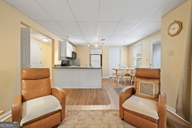 living area with a paneled ceiling, wood finished floors, and baseboards