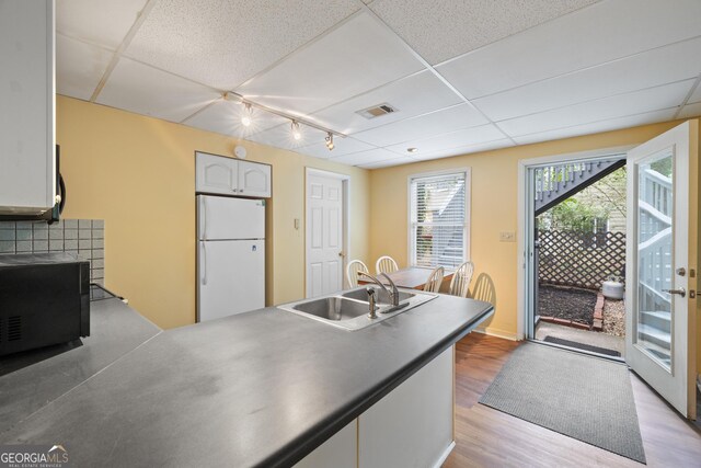 kitchen featuring freestanding refrigerator, a sink, black microwave, a paneled ceiling, and wood finished floors