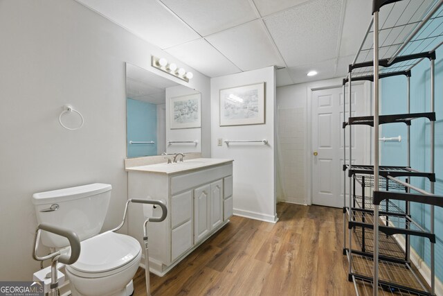 bathroom featuring toilet, a paneled ceiling, wood finished floors, recessed lighting, and baseboards