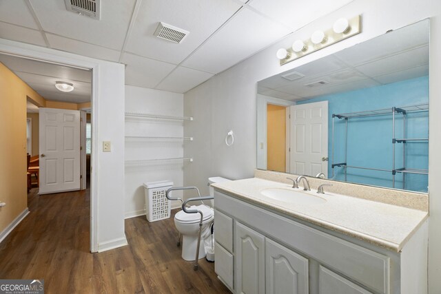 full bath featuring a paneled ceiling, wood finished floors, toilet, baseboards, and vanity