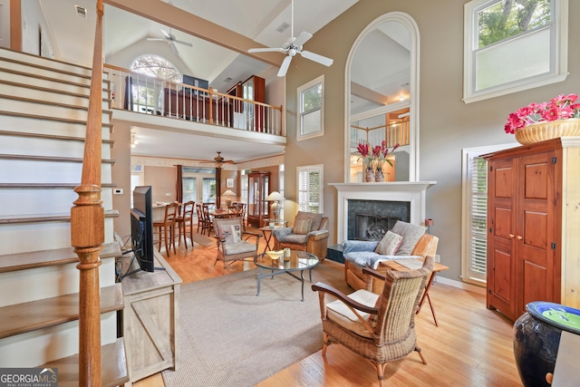 living room featuring ceiling fan, high vaulted ceiling, a fireplace, wood finished floors, and stairway