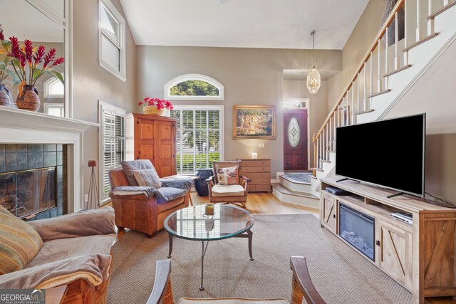 living room with stairs, a tile fireplace, a towering ceiling, and light wood-style floors