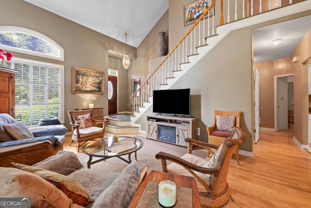 living area featuring high vaulted ceiling, stairs, light wood finished floors, and baseboards