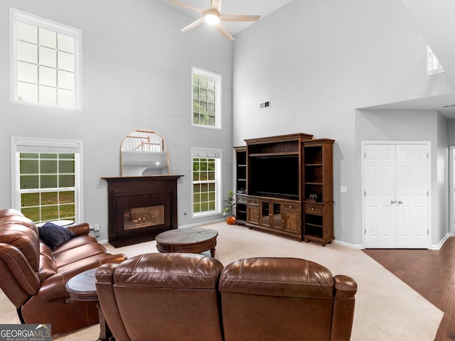 living area with high vaulted ceiling, ceiling fan, a fireplace with flush hearth, wood finished floors, and baseboards