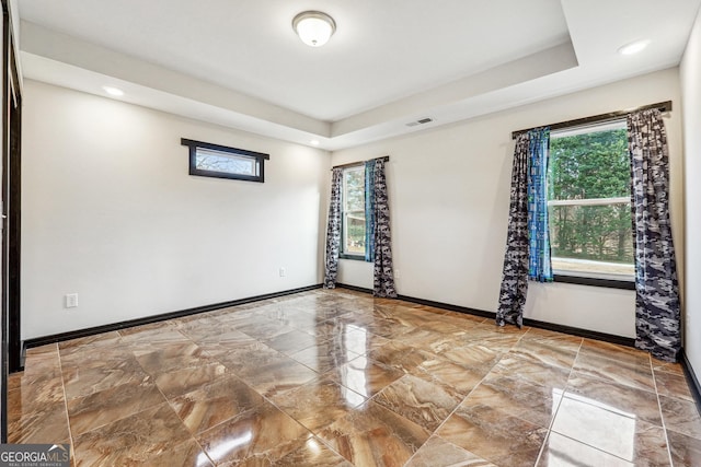 empty room featuring healthy amount of natural light, marble tiled floors, baseboards, a raised ceiling, and recessed lighting