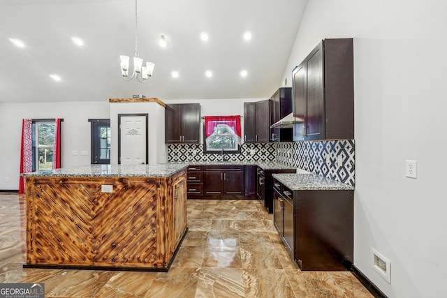 kitchen featuring light marble finish floors, lofted ceiling, a kitchen island, backsplash, and a chandelier