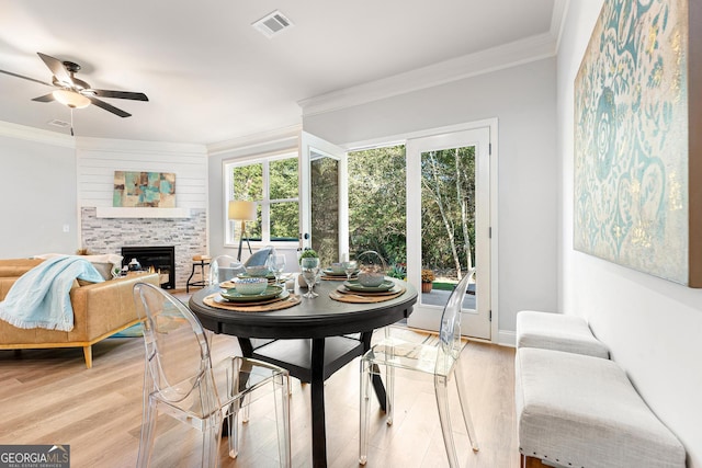 dining space with ceiling fan, crown molding, light wood-type flooring, and a stone fireplace