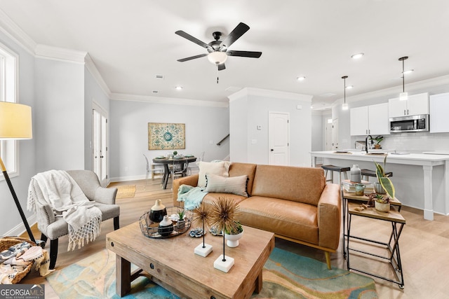 living room with crown molding, ceiling fan, light wood-style floors, baseboards, and recessed lighting