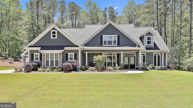 craftsman-style house with a chimney, a front yard, stone siding, and covered porch