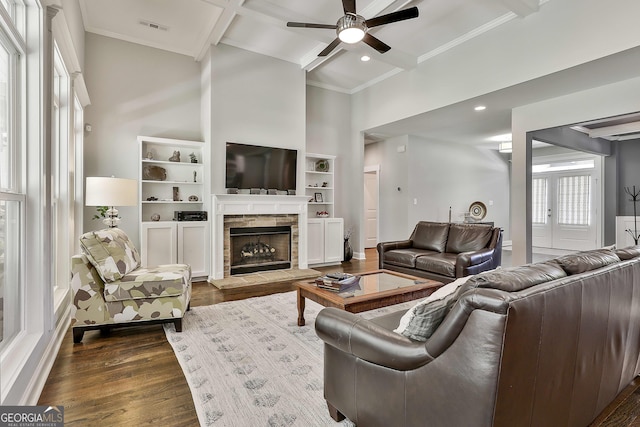 living area featuring a towering ceiling, ceiling fan, dark wood-style flooring, ornamental molding, and a fireplace