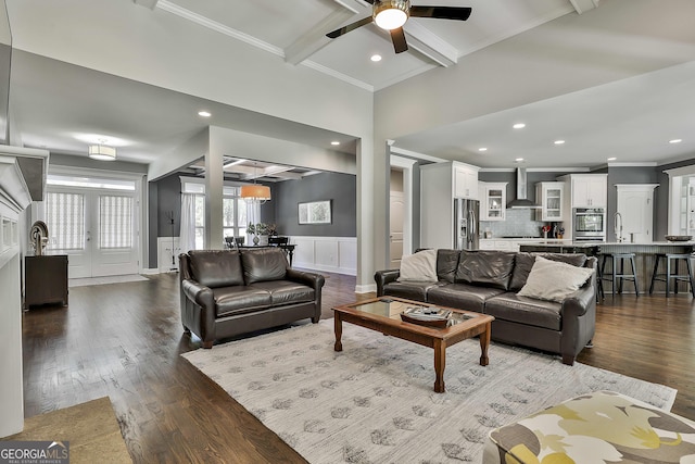 living room with beam ceiling, crown molding, wood finished floors, a ceiling fan, and a decorative wall