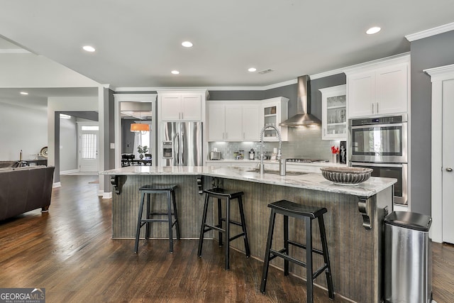 kitchen featuring wall chimney range hood, appliances with stainless steel finishes, a sink, backsplash, and dark wood-style floors