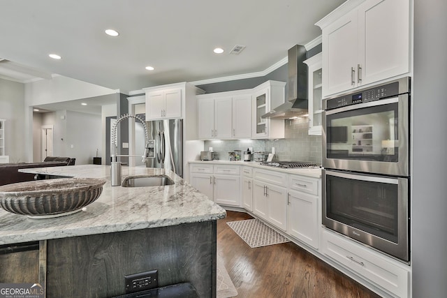 kitchen featuring wall chimney range hood, appliances with stainless steel finishes, ornamental molding, light stone counters, and white cabinetry