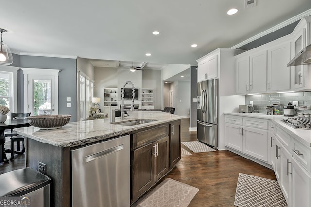 kitchen with stainless steel appliances, a sink, an island with sink, white cabinets, and ornamental molding